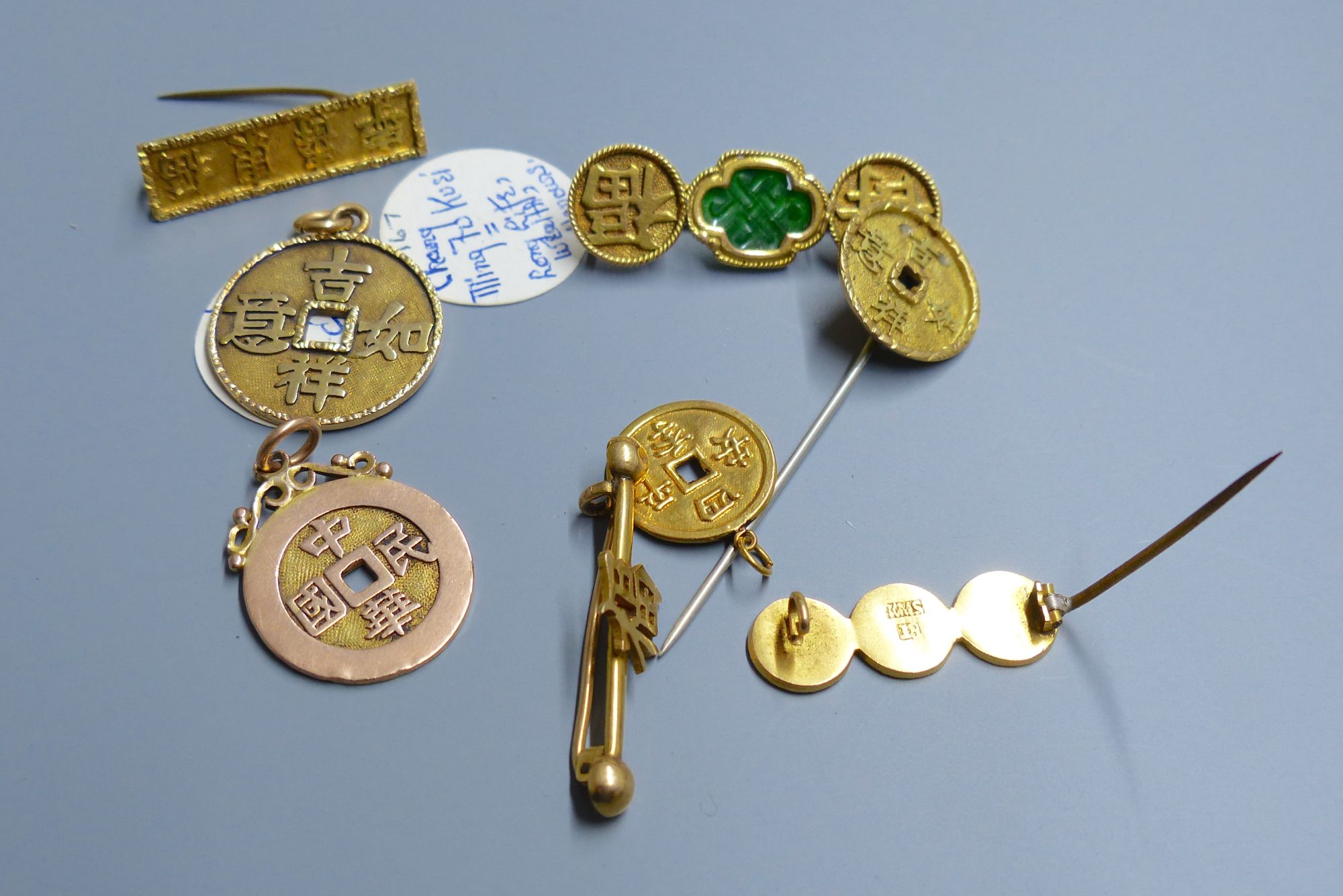 Eight assorted Chinese yellow metal amulets, four in the form of brooches, three pendants and a stick pin, 21.5 grams.
